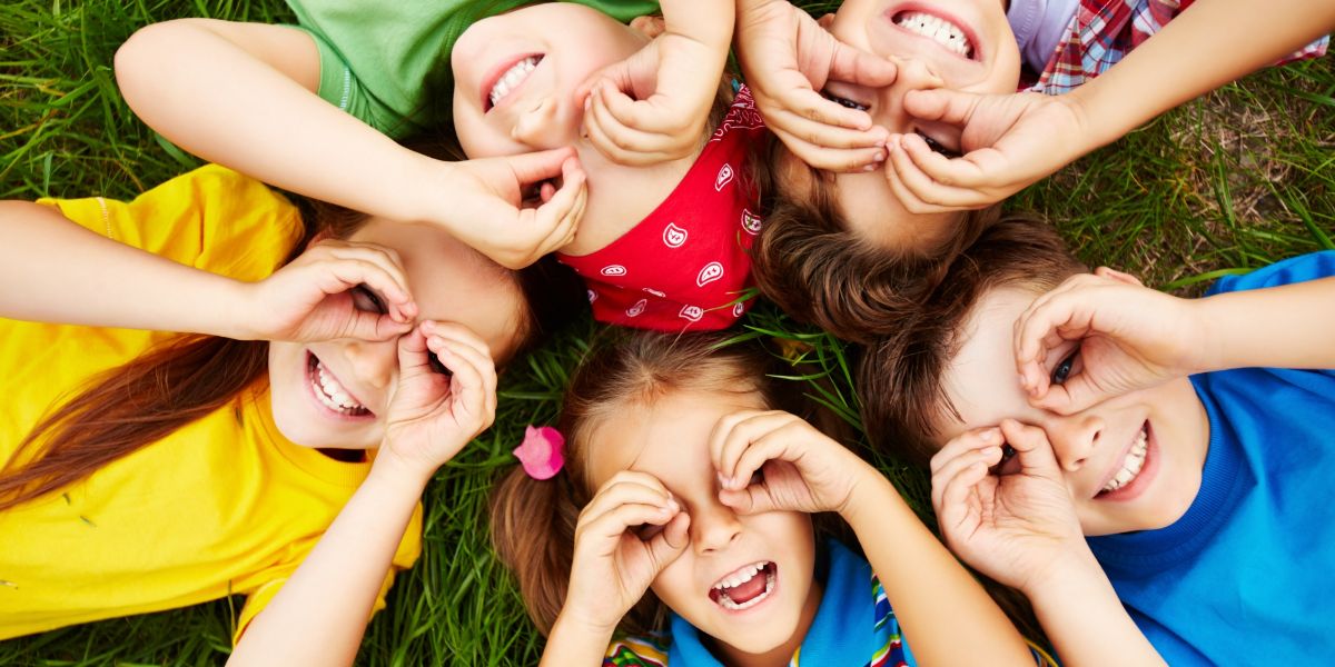 foto dall'alto di 5 bambini su un prato con le mani vicino agli occhi imitando la forma degli occhiali