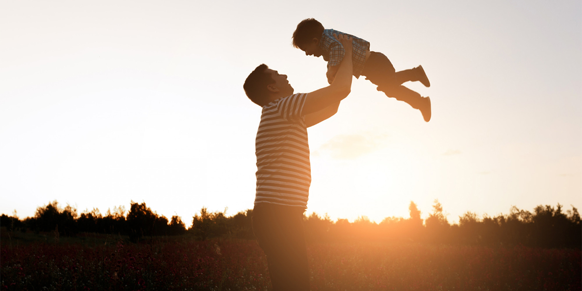 papà che tiene il figlio in braccio in aria con il tramonto in sottofondo
